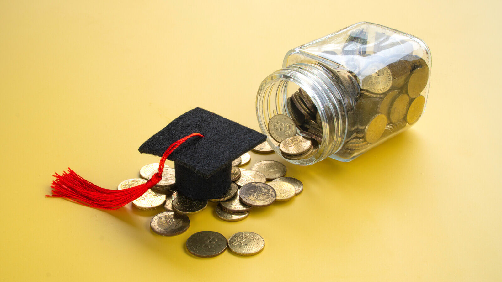Coins pour out of a jar onto a cap and tassel on a yellow background