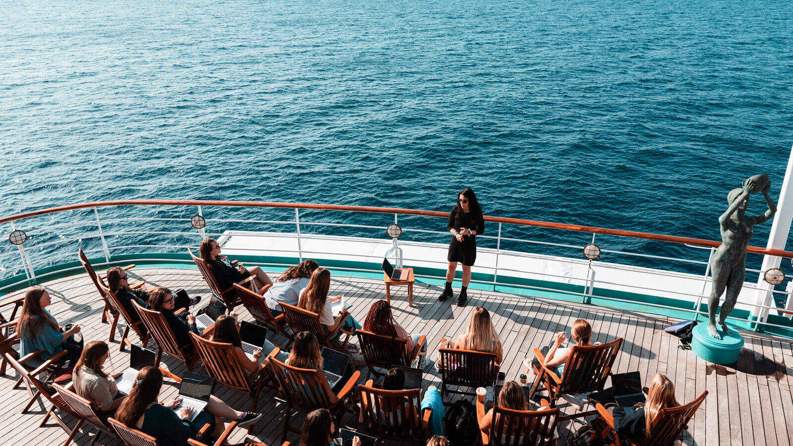 students sit at the aft of a ship listening to a college lecture