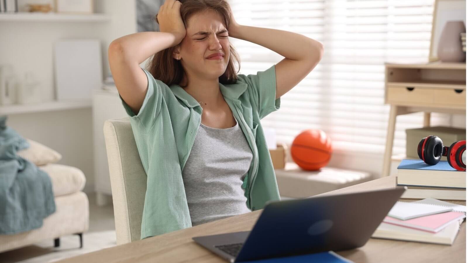 Stressed student sitting at desk grabbing head and staring at laptop trying to pick her right-fit college
