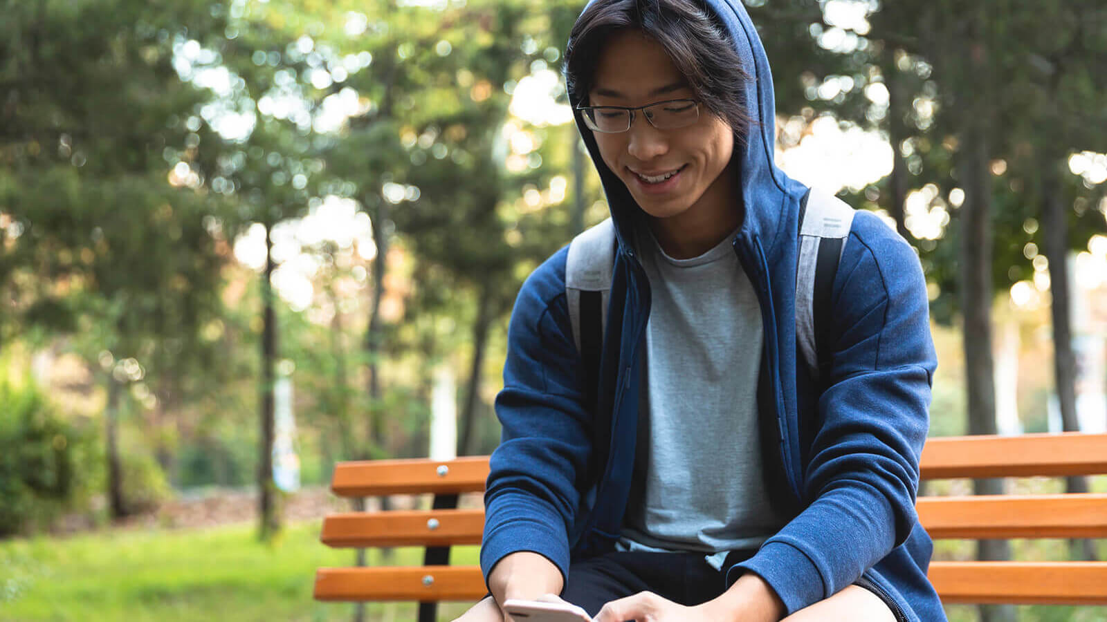 a young man sits on a park bench looking at his phone