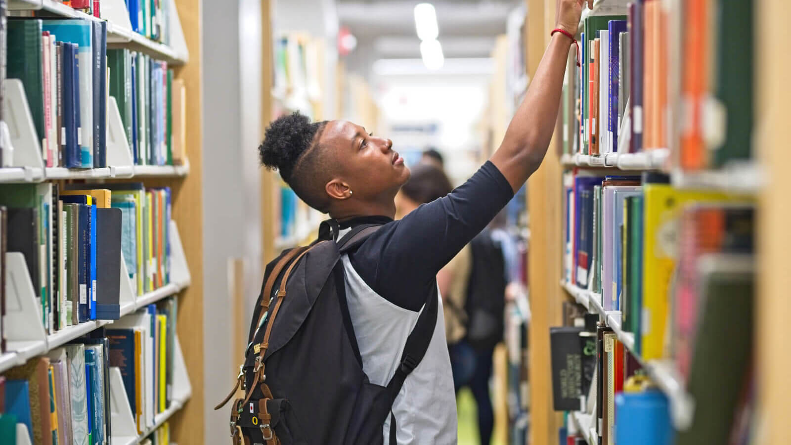 a student reaches up for a library book on a tall shelf