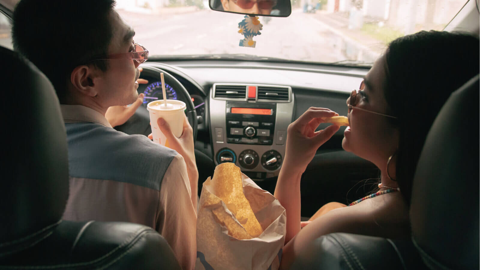 A young man and woman eating fast food in a car.