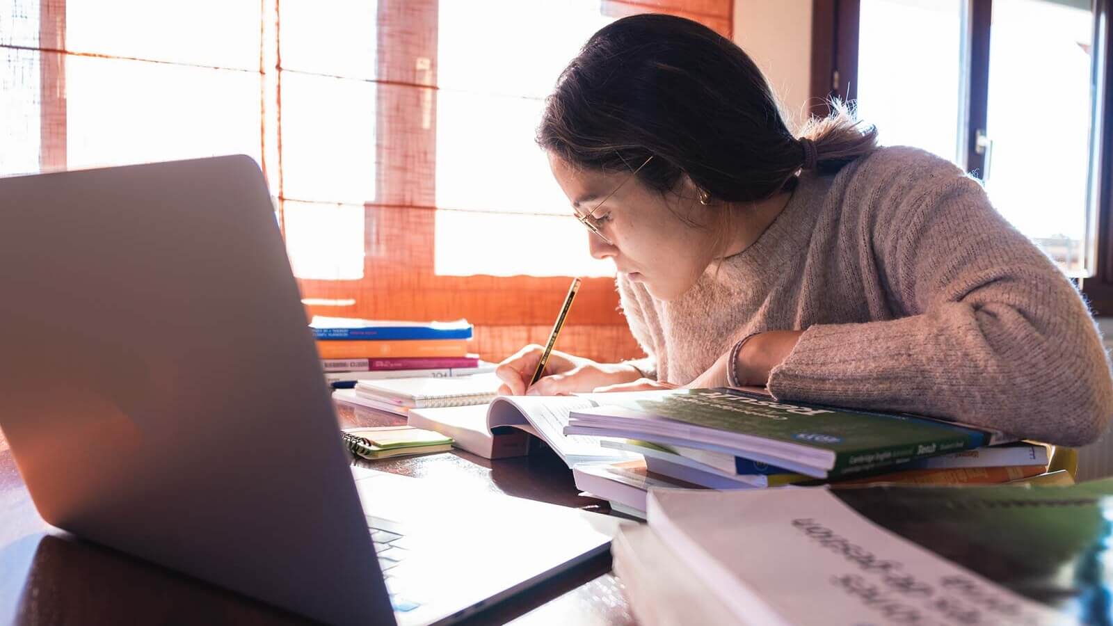 a student focusing on school work with book, laptop, and notebooks on a desk