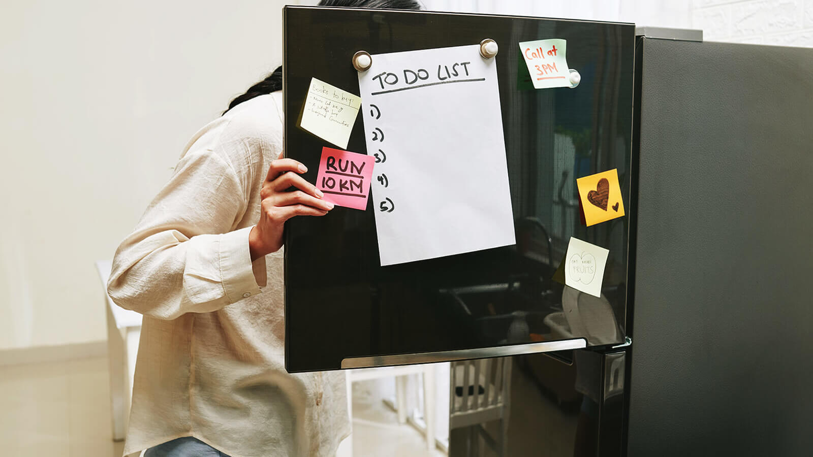 a student looks inside of a refrigerator with a to do list hanging on the door. 