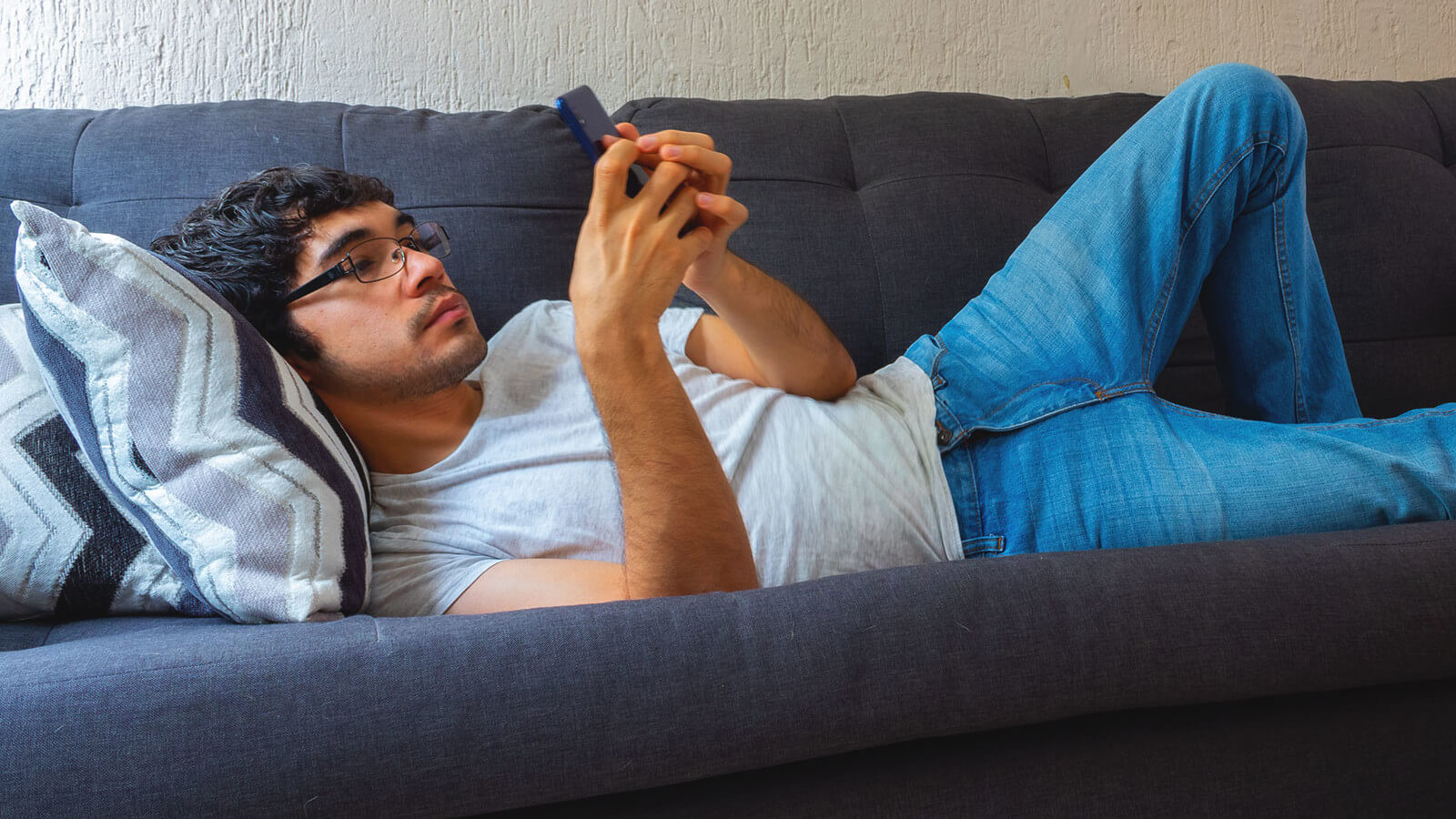 a young man researching scholarships on his phone while lounging on a sofa