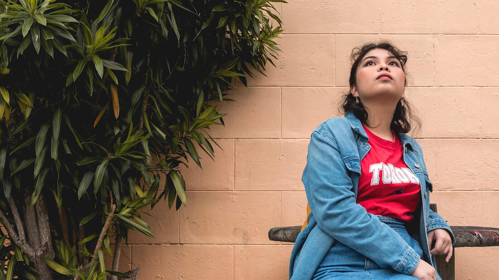 A young woman sitting outside looking up.