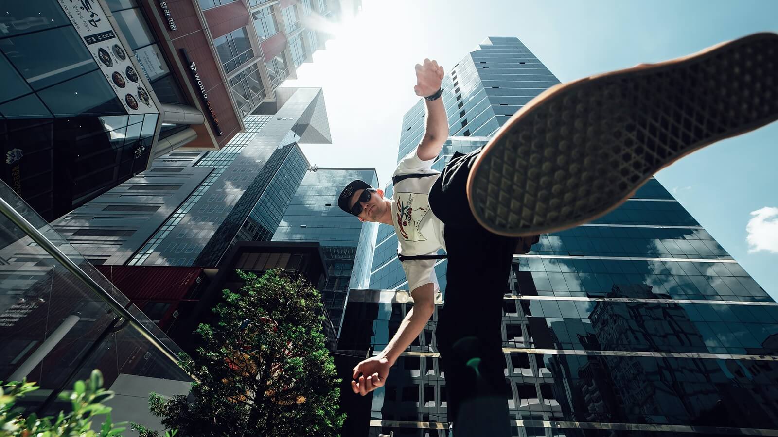 An upward shot of a city with a young man jumping upwards. 