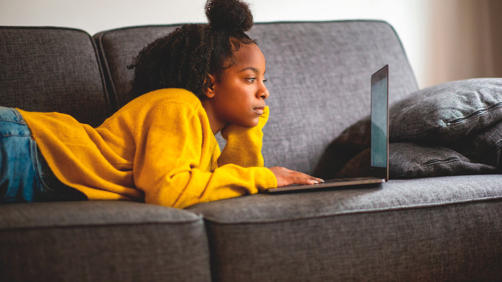 Student laying on couch reviewing her FAFSA submission on a laptop.