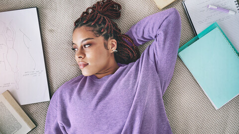 a young woman lays on her floor and looks off into space