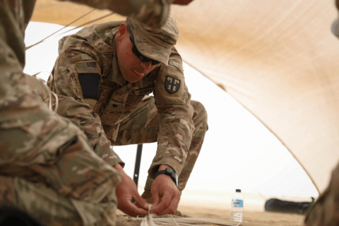 Army soldiers in BDUs work on setting up an tent