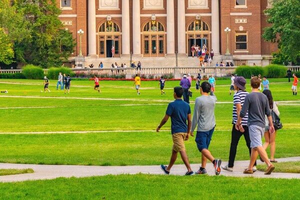 groups of students walking across a college campus quad lawn