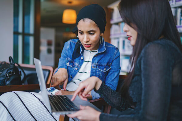 two young women review financial aid information on a laptop