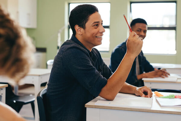 a young man sits in class with his pencil raised