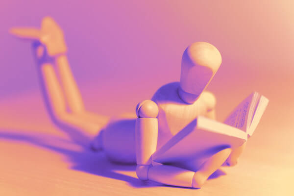a wooden figurine lays on his stomach and reads a book