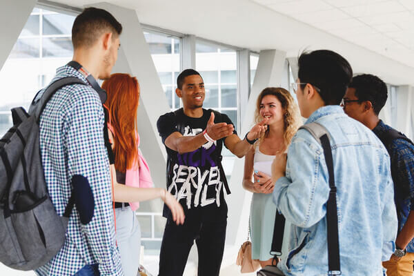 A young man leading a group tour and engaging with a group of students.