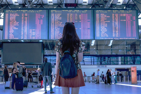 a young woman looks up at a flight tracker board in an airport