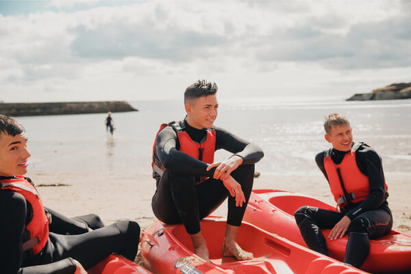 three male students sit on kayaks
