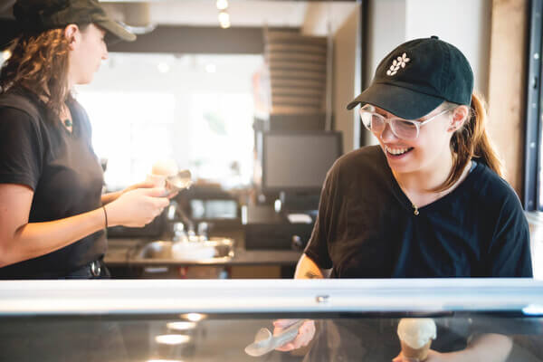 A young woman smiling while scooping ice cream behind a counter.