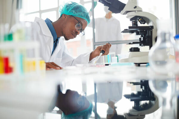 a student in scrubs conducts a test with a microscope and lab equipment