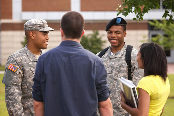 Two service members chatting with other students on a college campus.