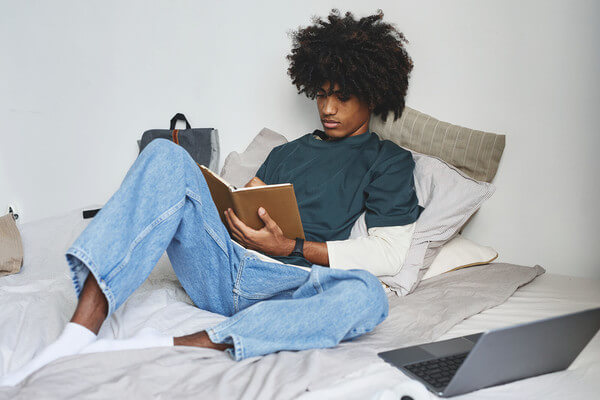 a boy student sits on his bed and studies for the AP exam