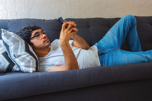 a young man researching scholarships on his phone while lounging on a sofa