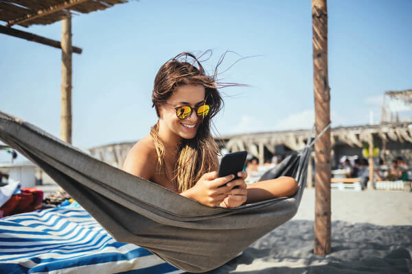 a student sits on a hammock on the beach reading on her phone