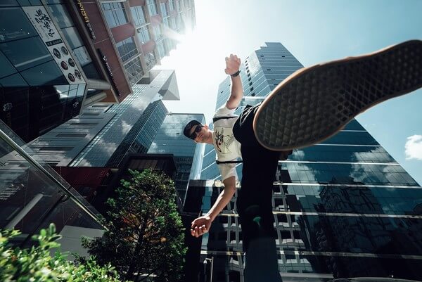 An upward shot of a city with a young man jumping upwards. 