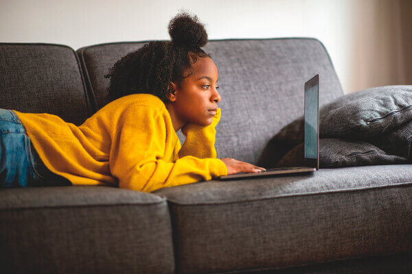 Student laying on couch reviewing her FAFSA submission on a laptop.