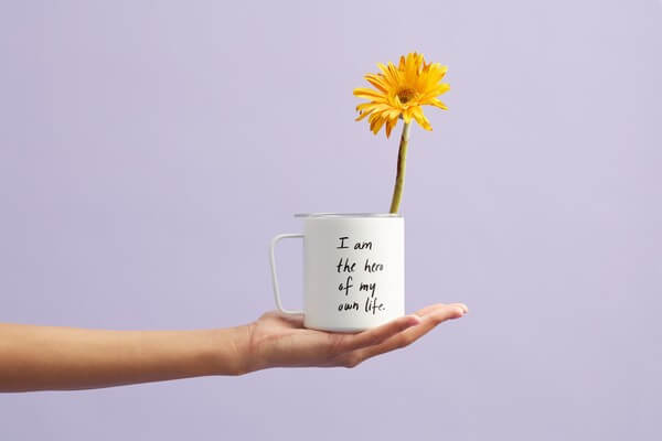 A person holding a mug with a yellow flower in a white mug.