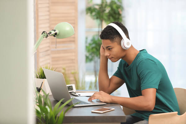 a male student applies for colleges on his laptop wearing headphones