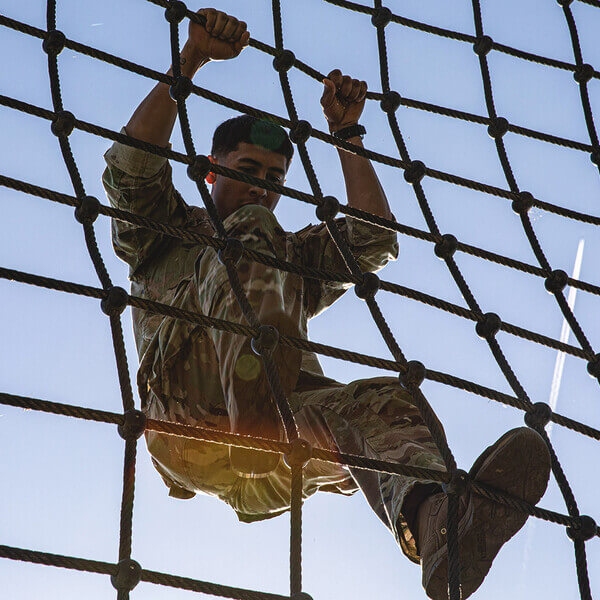 An ROTC cadet climbs a rope net in field training