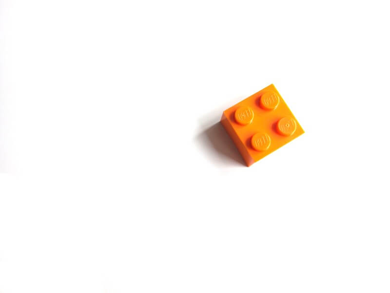 A single orange lego sits, face up, on a white background. 