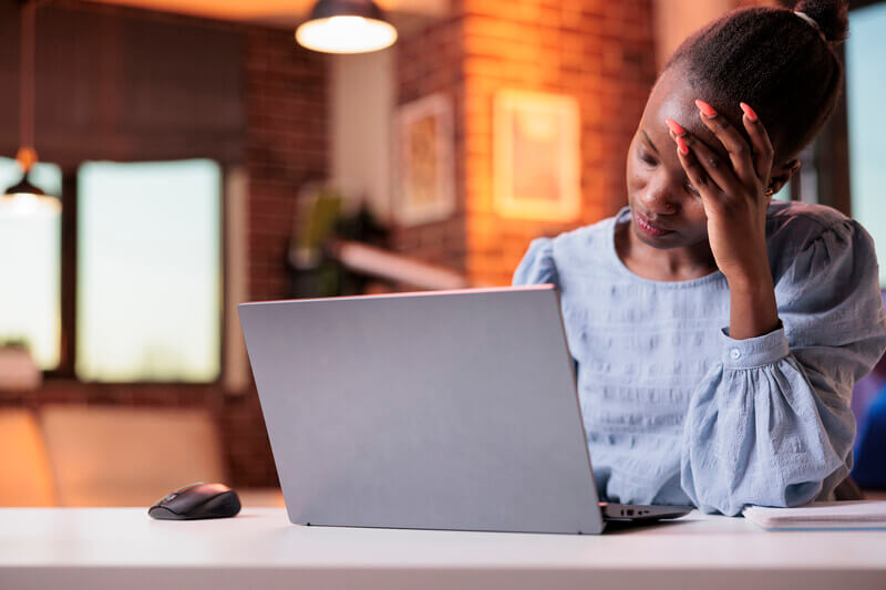 Tired woman on a laptop with her hand on her forehead.