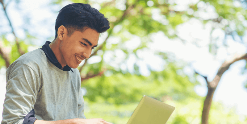 A man seated in a park with a laptop on his lap