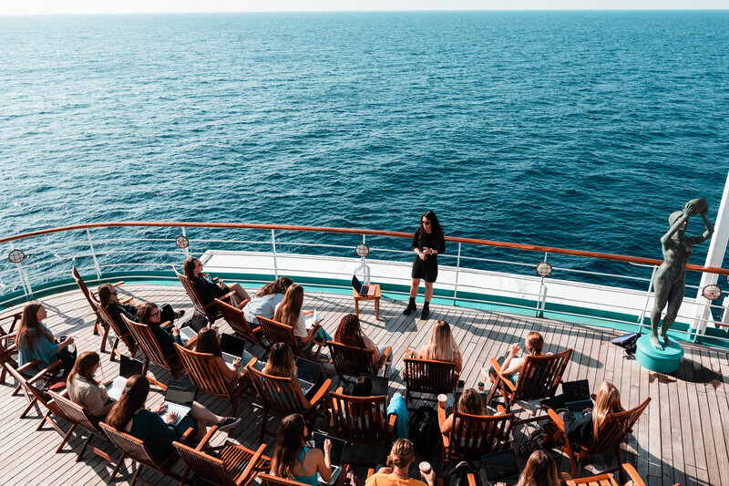 students sit at the aft of a ship listening to a college lecture