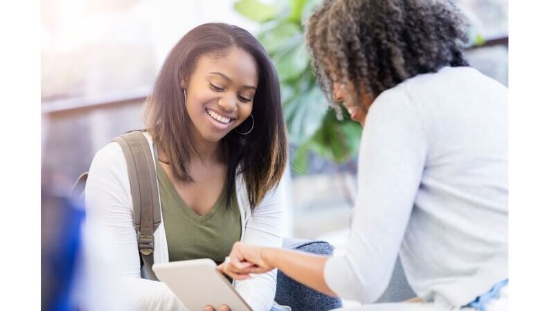 Smiling female student looking at a notebook and talking with her school counselor
