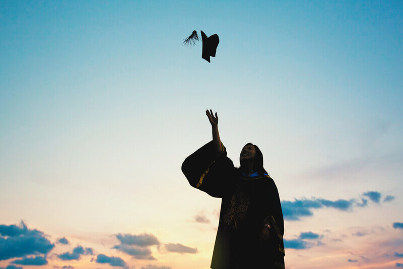a student throws their graduation cap up in the air
