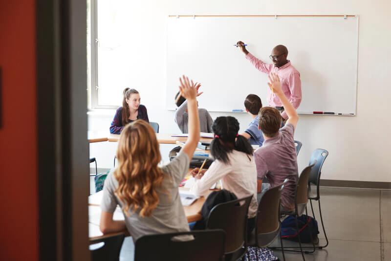 a teacher stands at the front of a high school classroom