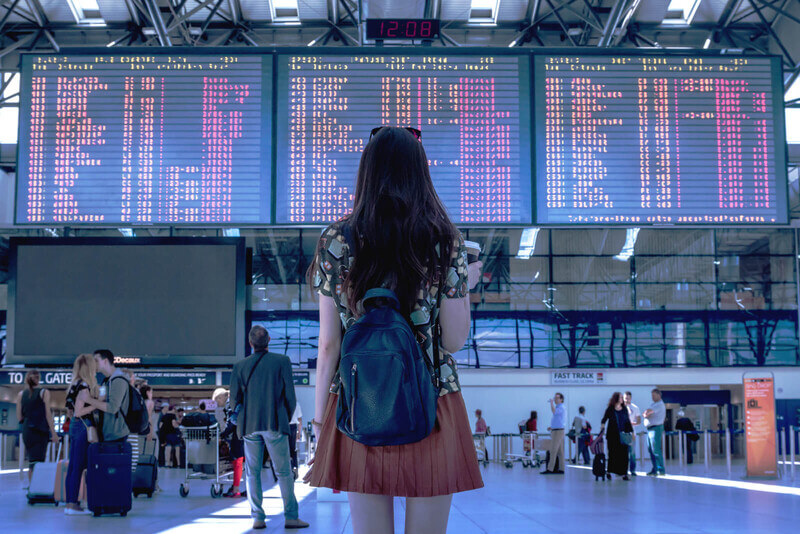 a young woman looks up at a flight tracker board in an airport