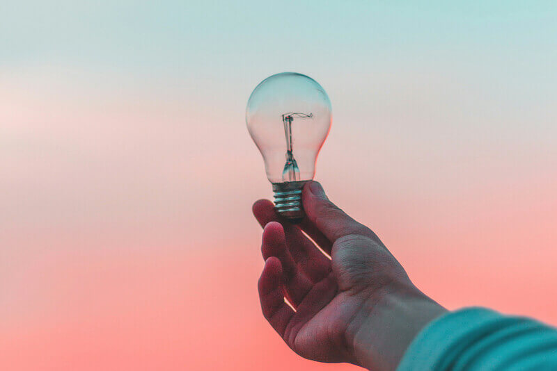 a hand holds up a light bulb with a sunset backdrop