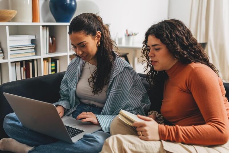 A mom and daughter sitting on a couch looking at a laptop
