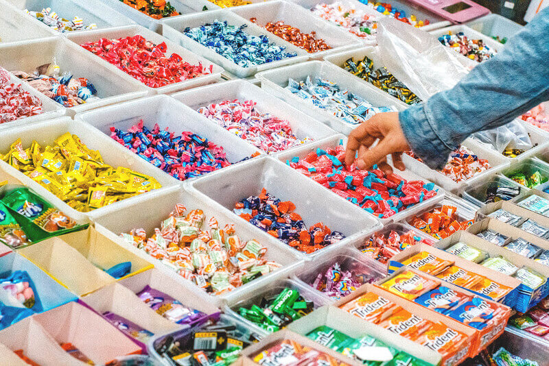 An arm reaching for a piece of candy from one of many assorted candy bins.