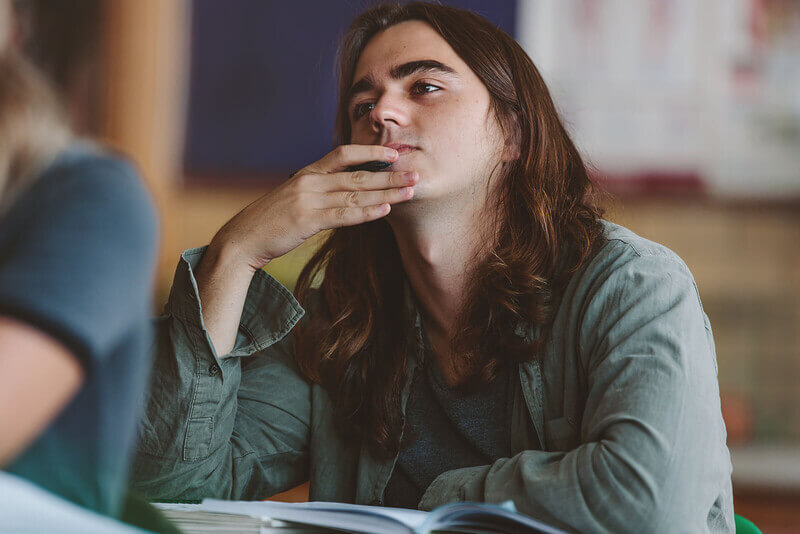 A male student holds his chin and looks off in introspection