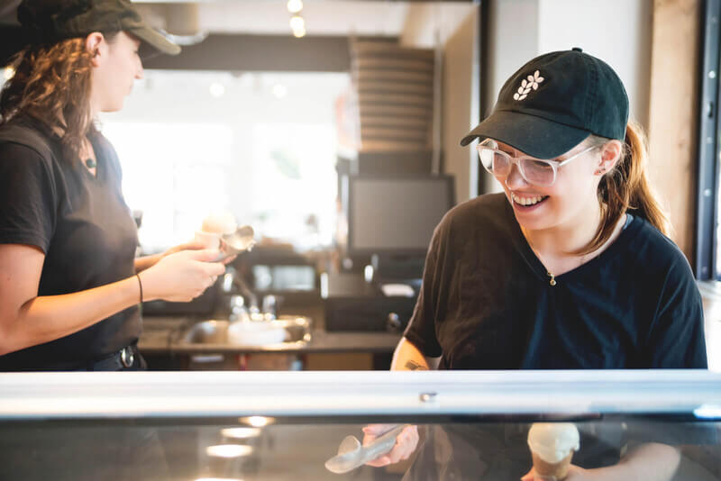 A young woman smiling while scooping ice cream behind a counter.