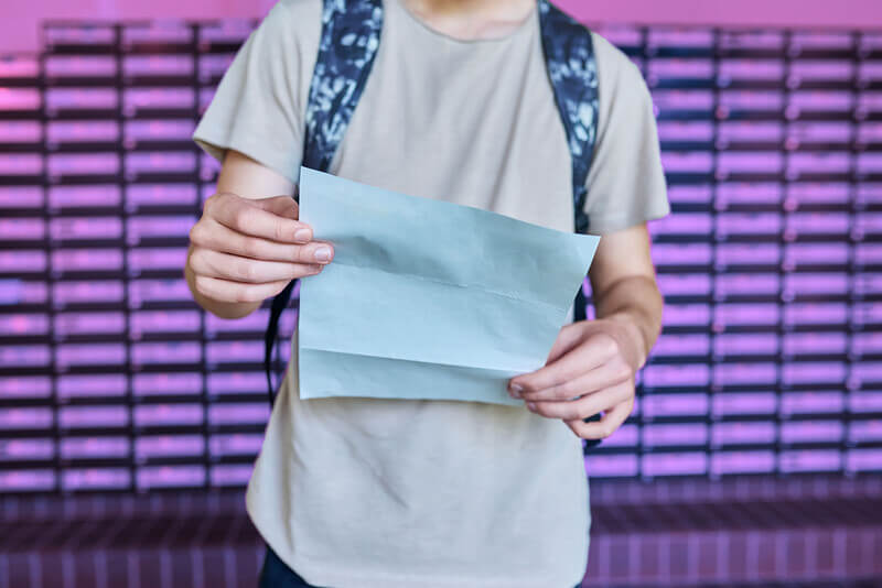 A student wearing a backpack holding a letter.