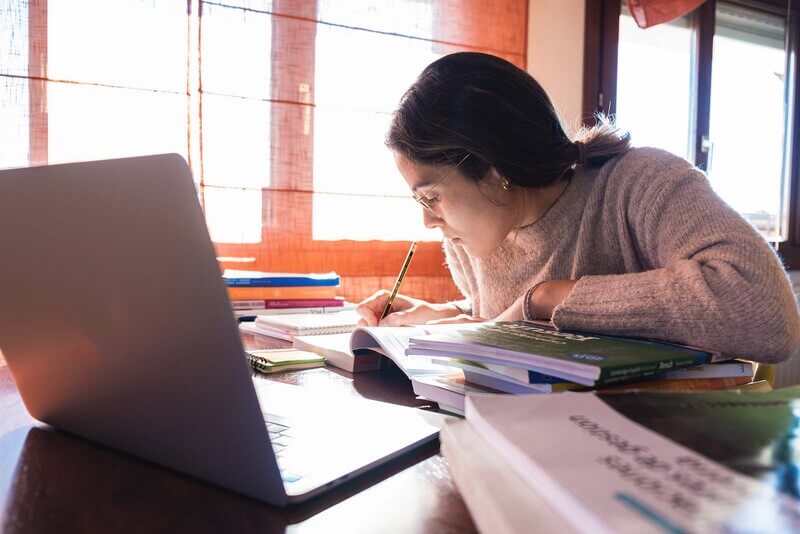 a student focusing on school work with book, laptop, and notebooks on a desk
