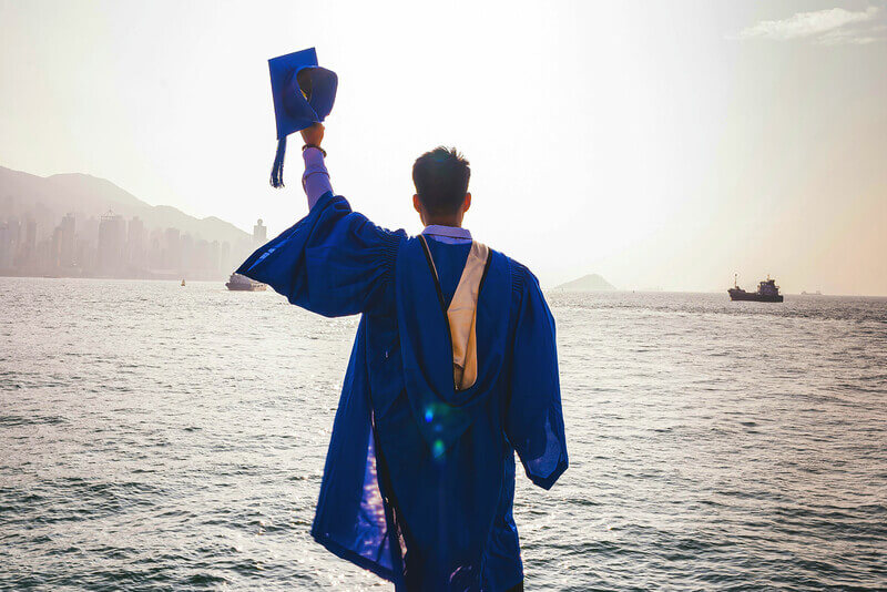 a college graduate in a gap and gown celebrates looking over the ocean