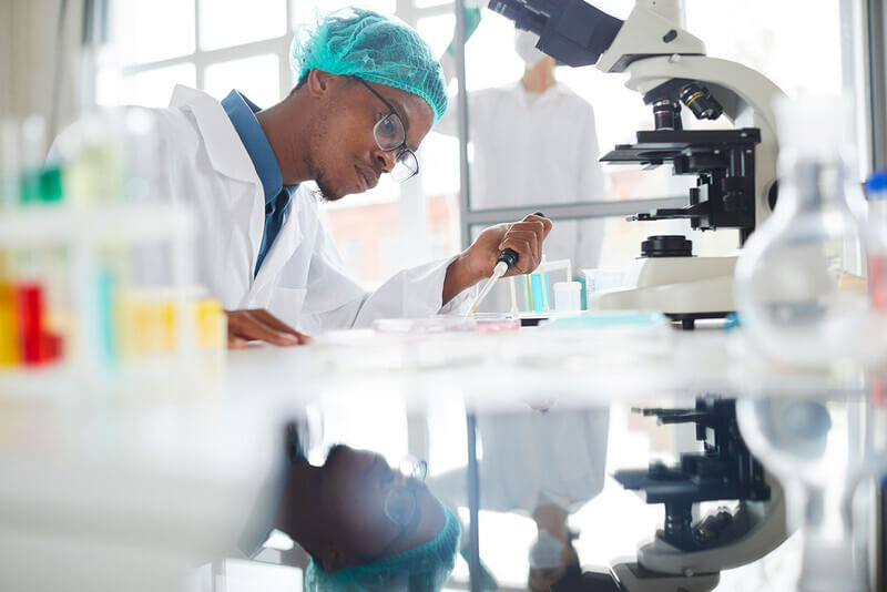 a student in scrubs conducts a test with a microscope and lab equipment