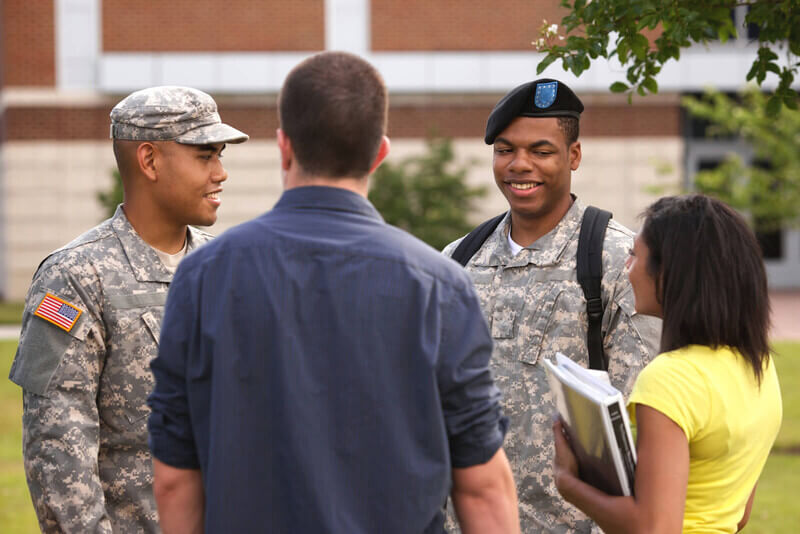 Two service members chatting with other students on a college campus.